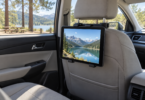 A black tablet showing a mountain lake mounted behind a car’s front passenger headrest.
