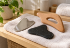 Generic metal, dark stone and wooden body massage tools arranged on a linen towel beside a plant