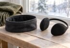 Charcoal fleece headband and black ear warmers on a wooden bench beside a winter window