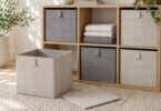 Unbranded gray and oatmeal fabric storage bins in a wooden shelving unit, with an empty bin and a flat support panel on the floor