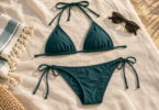 Illustration of a generic teal triangle bikini top and tie-side bottom laid flat on cream linen beside a towel and sunglasses