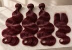 Three unbranded burgundy wavy hair bundles and a matching lace closure arranged on a light stone tabletop