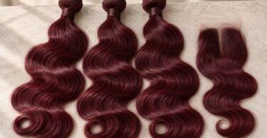 Three unbranded burgundy wavy hair bundles and a matching lace closure arranged on a light stone tabletop