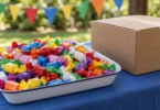 Colorful wrapped candies in a tray beside a plain supply box on a shaded outdoor table