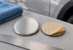 Blank silver automotive medallion beside an adhesive backing, ruler and blue microfiber cloth