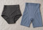 A charcoal high-waisted brief and slate-blue shaping shorts laid flat on pale gray fabric