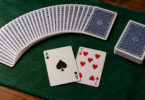 An unbranded fan of blue-backed playing cards, a squared deck and two face-up cards on a green mat.
