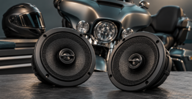 Two generic round speakers on a workbench with a parked touring motorcycle and helmet in the background.