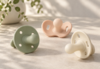 Conceptual illustration of sage, peach and ivory pacifiers with vented shields on a clean tabletop.