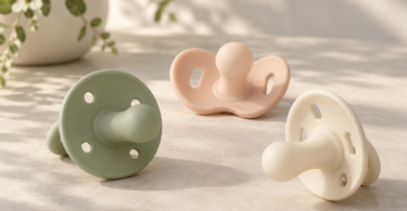 Conceptual illustration of sage, peach and ivory pacifiers with vented shields on a clean tabletop.