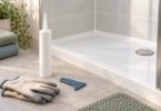 Conceptual image of an unbranded sealant cartridge, finishing tool and gloves beside a dry tiled shower tray.