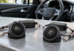 Two generic black automotive tweeters and inline crossovers on a workbench beside a car interior