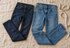 Two pairs of unbranded blue jeans laid on beige fabric beside a measuring tape