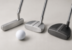 Three unbranded silver and charcoal golf putters with different head shapes beside a white golf ball on a neutral studio surface