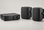 Unbranded black stereo amplifier beside two passive speakers with mounting brackets on a neutral studio background