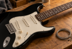 Black electric guitar with a cream pickguard beside coiled metal guitar strings on a wooden workbench