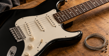 Black electric guitar with a cream pickguard beside coiled metal guitar strings on a wooden workbench