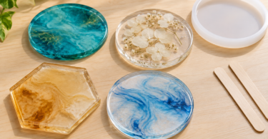 Four translucent resin coasters in teal, clear floral, amber and pale blue designs beside an empty white mold and two wooden mixing sticks