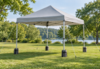 Unbranded light gray folding canopy on a lawn with guy ropes, ground stakes and weight bags at its four legs