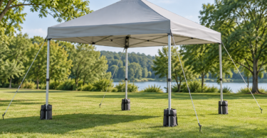 Unbranded light gray folding canopy on a lawn with guy ropes, ground stakes and weight bags at its four legs