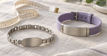 A silver link bracelet and a lavender silicone bracelet with blank metal plates beside a fabric measuring tape on linen.