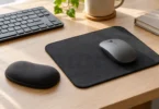 A gray mouse on a dark fabric mouse pad with a separate rounded support on a light wood desk