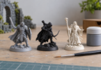 Gray, black and off-white fantasy miniatures beside a paintbrush and closed paint pot.