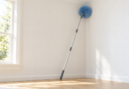 A generic blue cobweb brush on a silver telescoping pole leaning against a white interior corner.