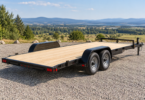 Empty unbranded black tandem-axle car-hauler trailer with a wood deck parked on a gravel lot.