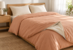 A bed with plain peach bedding, two cream pillows and a folded corner showing a light lining and zipper.