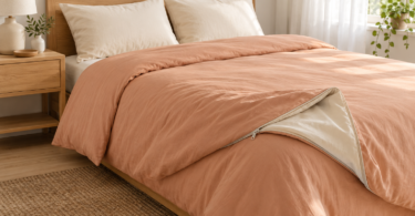 A bed with plain peach bedding, two cream pillows and a folded corner showing a light lining and zipper.