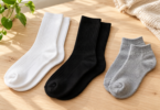 Three pairs of plain white, black and grey knit socks arranged on a wooden table.