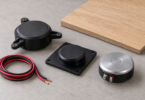Illustration of three unbranded surface exciters, disconnected speaker wire and a wood panel on a workbench