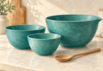 Illustration of three teal mixing bowls and a wooden spoon on a light kitchen countertop.